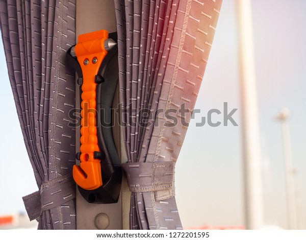 Orange safety hammer mounting\
near the window glass and curtain on the bus, use in case\
accident.