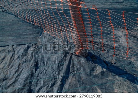 Orange safety netting delineating a construction or landscaping area with weed barrier fabric on ground