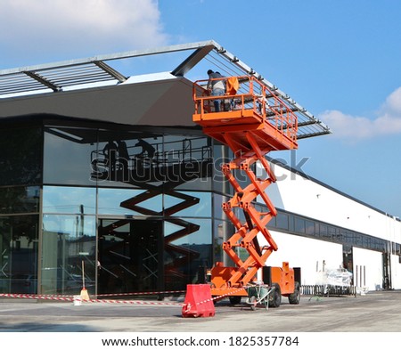 Orange scissor lift, a type of aerial platform, at work on a building facade under construction
