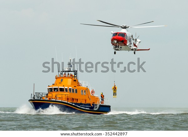 orange sea rescue boat at\
sea off south coast of Britain man being winched to emergency\
rescue helicopter