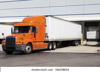 Orange Semi Truck By The Door Of Warehouse