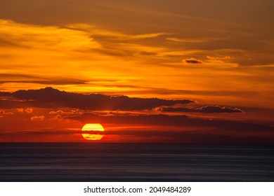 The orange setting sun in the clouds over the dark sea.