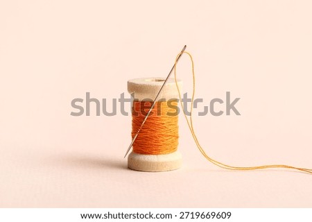 Orange sewing thread with needle on beige background