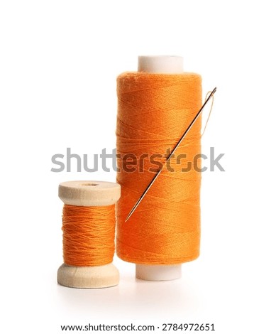 Orange sewing thread spools with needle isolated on white background, closeup