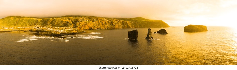 Orange sky sunset above ocean and Mosteiros village on Sao Miguel Island. Hills and cliffs before storm. Wide panoramic aerial drone view. Azores, Portugal. - Powered by Shutterstock