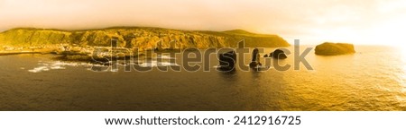 Orange sky sunset above ocean and Mosteiros village on Sao Miguel Island. Hills and cliffs before storm. Wide panoramic aerial drone view. Azores, Portugal.