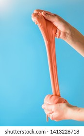 Orange Slime Stretch Two Hands On A Turquoise Background. Toy Antistress. Toy For The Development Of Hand Motor Skills.