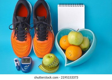 Orange Sneakers, Diary Notebook, Glucometer, Measuring Tape And Fruits On A Blue Background. Body Weight Control. Blood Glucose Control