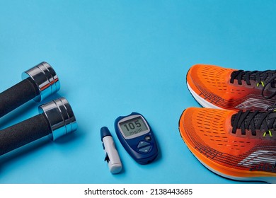 Orange Sneakers, Metal Dumbbells And A Blood Glucose Meter On A Blue Background. Exercise To Overcome Insulin Resistance