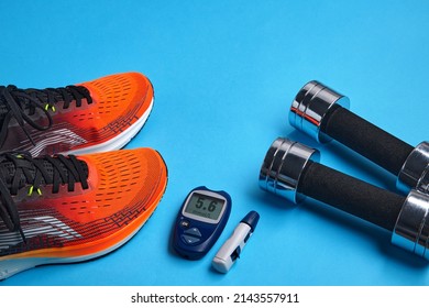 Orange Sneakers, Metal Dumbbells And A Blood Glucose Meter On A Blue Background. Exercise To Overcome Insulin Resistance