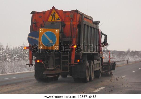 Orange snow blower sweeper truck drive\
on suburban winter asphalt road on snowy trees background at winter\
day - municipal highway snow cleaning\
service