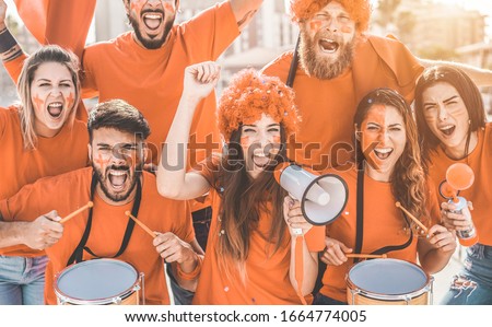 Orange sport fans screaming while supporting their team out of the stadium - Football supporters having fun at competion event - Champions and winning concept - Focus on center girl face