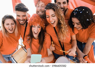 Orange sport supporters watching football game on mobile phone - Main focus on center girl face