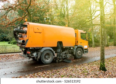 Orange street sweeper machine cleaning the street after in fall from fallen foliage on a sunny day