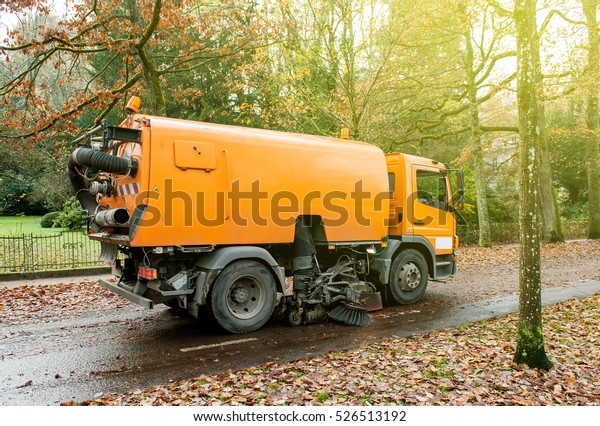 Orange street sweeper\
machine cleaning the street after in fall from fallen foliage on a\
sunny day
