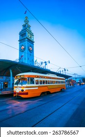 An orange street tram / train in downtown San Francisco at twilight.