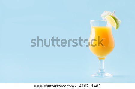 Orange summer alcoholic cocktail with mango juice, rum, liqueur, lime and ice, blue background, copy space