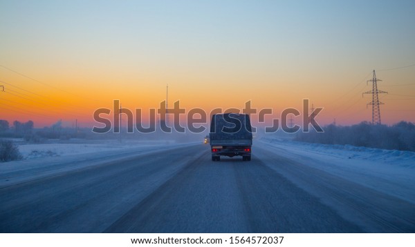 Orange\
sunrise, winter road, rear view of the vehicle without visible\
logos and power transmission towers in\
winter