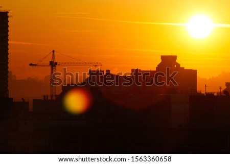 Orange sunset on the background of the city. Silhouette of a construction crane. Photo with a glare from the sun. Panorama of the city.

