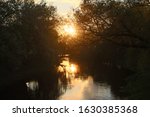 Orange sunset over the river between black bushes in spring. The sun is reflected in the channel of the riverbed