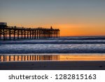 Orange sunset reflects of the surf and silhouettes Chrystal pier on Mission Beach in San Diego, California.