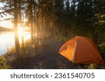 orange tent in a forest at the Yukon River in Canada during epic sunset