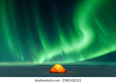 Orange tent lighted from the inside against the backdrop of incredible sky with Northern lights. Aurora borealis in winter field
