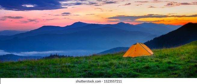 Orange tent in the mountains at sunset. The chamber stands on a hill in the green grass. Against the background of silhouettes of mountains and dramatic sky. Solitude and travel wildlife concept - Shutterstock ID 1523557211