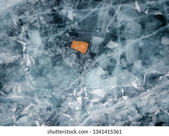 Orange Tent Mounted On Slippery Smooth Ice Of The Baikal Lake. Icy Plane Surface With Web Of Cracks, Snow Banks And Tent Dome. Aerial Top Down View.