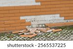 Orange tiles falling off a building facade and scattered on a cobblestone sidewalk, illustrating building damage and needed repairs