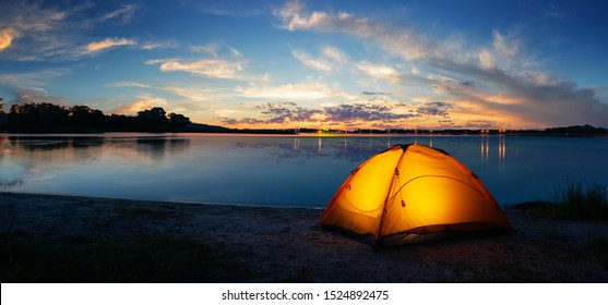 Orange tourist lit tent by the lake at sunset. Dramatic sky - Powered by Shutterstock
