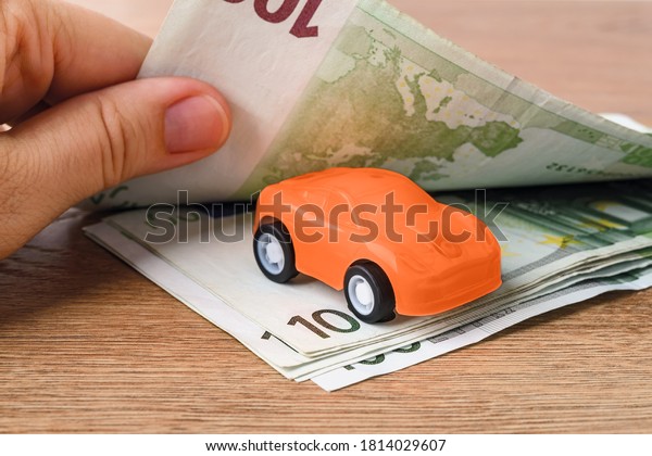 Orange toy car\
between 100 euro banknotes. Woman hands count paper money. Concept\
of car buying, renting, service, repair and insurance costs.\
Planning for expenses. Front\
view.