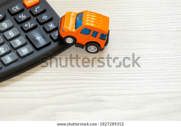 Orange toy car and calculator on table . Car buying,\
leasing,  car-sharing , car insurance concepts. Top view, flat lay,\
space for text .
