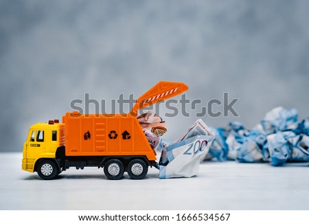 orange toy garbage truck unloads crumpled paper banknotes on a white table on a blue background. Money trash, free space Foto stock © 