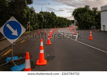 Orange traffic cones lined up on the road. Board with blue arrow pointing to the right to divert traffic. Auckland. 
