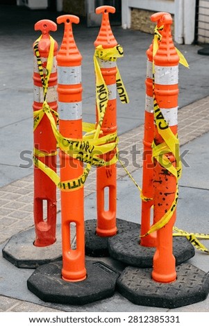 Orange traffic delineator posts wrapped in yellow caution tape on a city sidewalk. Construction zone safety barrier, roadwork warning signal, urban security, maintenance or hazard block.