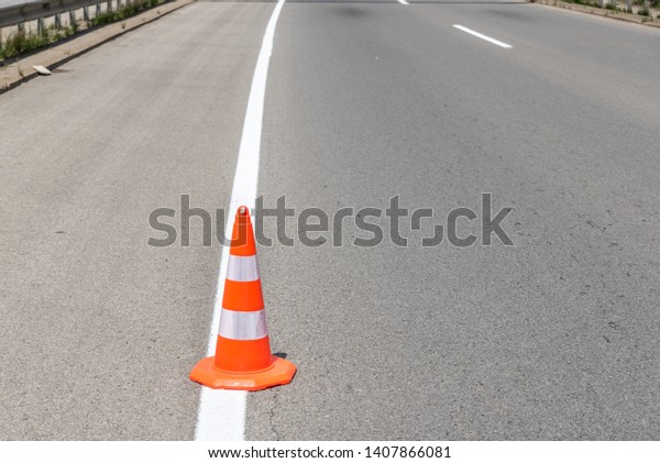 Orange traffic safety cone barrier on the  street\
protect fresh white paint marking on dividing asphalt road driving\
lanes low point of view