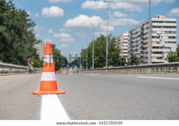 Orange traffic safety cone barriers on the street\
protect fresh white paint marking on dividing asphalt road driving\
lanes low point of view