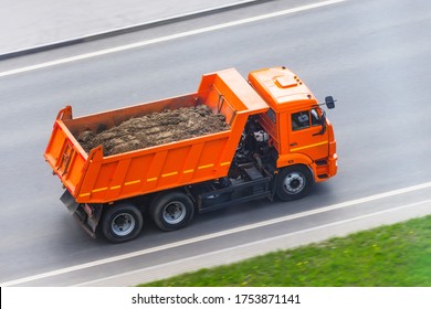 Orange truck dump with a load of soil in the body rides on the highway