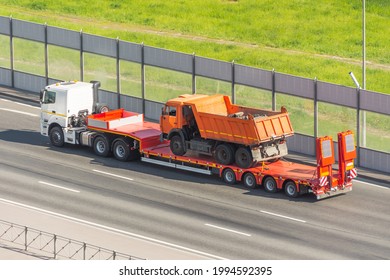 Orange truck dump with a load of soil in the body, transported on a trailer to the loading platform of another truck, help is broken breakdown evacuation