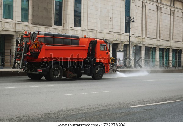 orange truck loaded with water barrels watering a\
roadway             