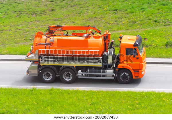 Orange truck with a tank and a water pumping\
system drives on the\
highway