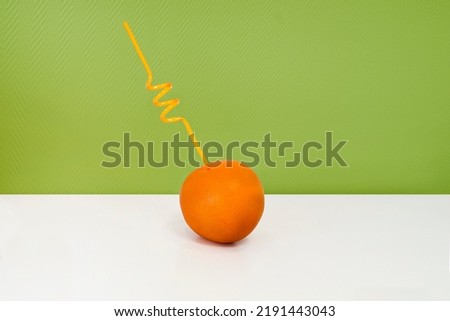 - An orange tube-straw in the form of a spiral is stuck in a whole juicy ripe grapefruit. Fruit on a white table against a juicy green wall. Fresh juice, the benefits of fresh fruit, fortified