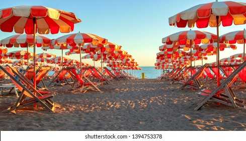 Orange Umbrellas Stand In Line On Italian Beach After Sunset In Cecina.