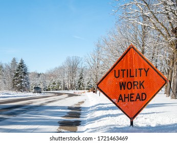 Orange UTILITY WORK AHEAD Sign Warns Traffic About A Work Zone On A Snowy City Street, On A Frosty And Sunny Winter Day In Bemidji, Minnesota.