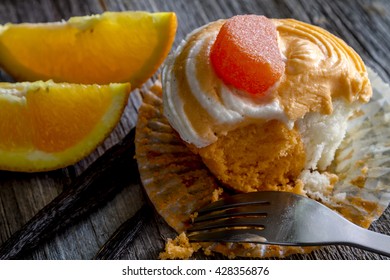 Orange and vanilla bean swirled cupcakes with candy garnish sitting on wooden table with fresh orange slices and vanilla bean pods and fork