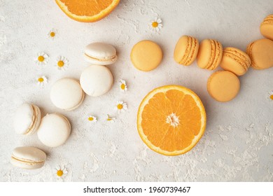 Orange and Vanilla French Macaroons with orange fruit filling on a creamy white clay background, decorated with small chamomiles and fresh sliced oranges