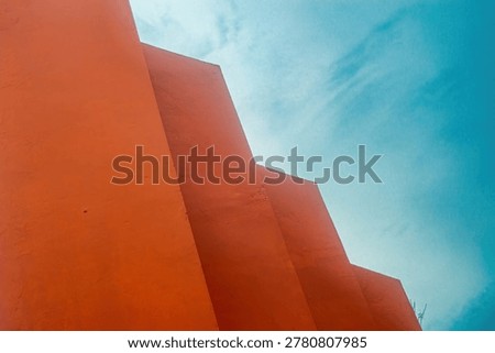 Orange wall forms a geometric composition against a vibrant blue sky, resembling an abstract stair pattern in urban architecture