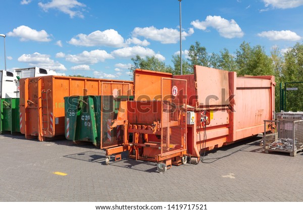 orange waste compactors are\
standing on a factory site with other waste containers next to\
them