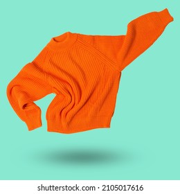 orange wool knitted sweater flies like a super hero, hand up, levitates on a light green background, concept - Shutterstock ID 2105017616